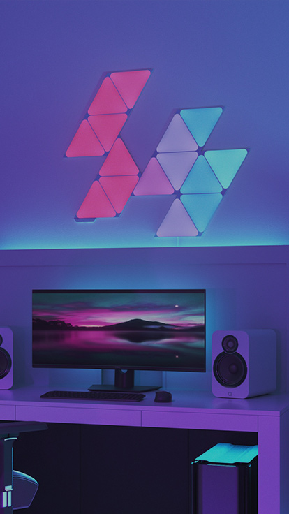 This is an image of a 15 panel layout of Nanoleaf Shapes Triangles on the wall above the desk and behind the monitor in a gaming battlestation. These RGB lights have over 16 million colors and are perfect for the gamer in your home.